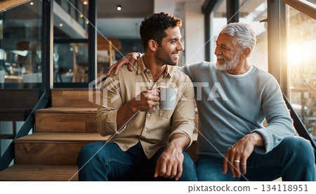 Two men share a moment on stairs while holding a coffee cup during morning light in a cozy cafe setting 134118951