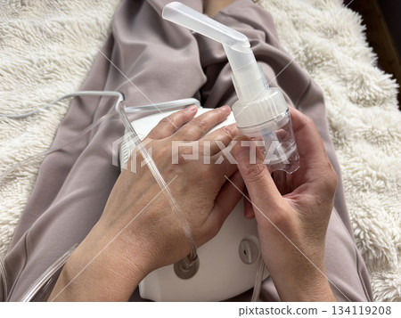 Close up of a portable electric nebulizer inhaler held in the hands of a sick adult woman at home, modern medical device for respiratory therapy, asthma and cold treatment equipment, healthcare 134119208