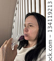 Adult woman using a home nebulizer inhaler while sitting in a cozy bedroom, respiratory treatment at home for breathing relief, healthcare and medical therapy concept, realistic lifestyle scene 134119213