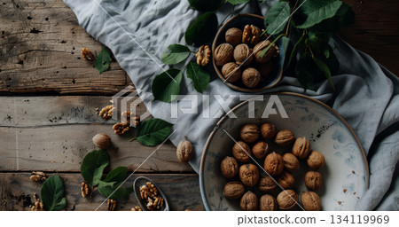 Freshly gathered walnuts in a bowl sit alongside vibrant green leaves on a weathered wooden tabletop, creating a natural display 134119969