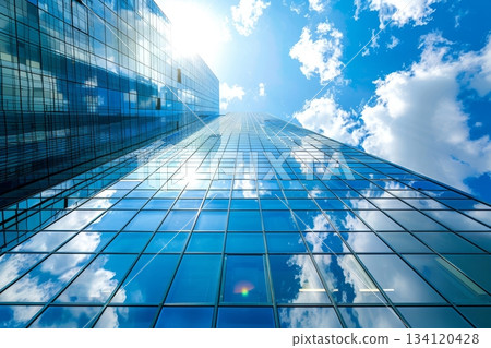A tall skyscraper with reflective glass surfaces towers against a bright blue sky filled with white clouds, capturing the beauty of a sunny day 134120428
