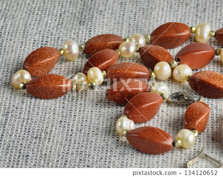 A stylish handmade pearl and aventurine necklace lying on burlap. Close-up 134120652
