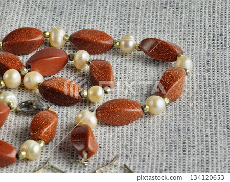 Stylish handmade pearl and aventurine necklace lying on burlap. Close-up 134120653