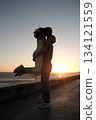 Man lifting woman in joyful embrace by the sea at sunset, romantic silhouette moment filled with love and happiness. 134121559