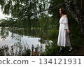 Elegance by the Lake: Woman in White Off-Shoulder Dress Among Birch Trees 134121931