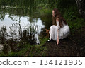 Contemplation by the Water: Woman in White Dress Gazing at the Lake 134121935