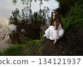 Contemplation by the Water: Woman in White Dress Gazing at the Lake 134121937