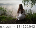Contemplation by the Water: Woman in White Dress Gazing at the Lake 134121942