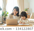 A mother working from home and her child doing homework. Parents and children spending time together smiling in a bright living room. 134122807