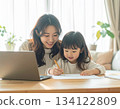 A mother working from home and her child doing homework. Parents and children spending time together smiling in a bright living room. 134122809