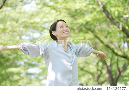 A woman in her 40s taking a deep breath outdoors A woman in her 40s taking a deep breath outdoors 134124277