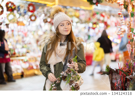 Girl with cone and fir brunch garland stands in middle fair decorated for New Year holidays 134124318