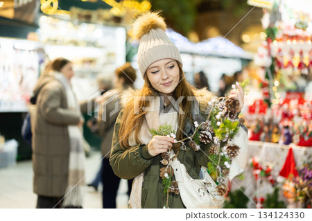 Girl looks at garland made of fir cones and brunchs, Xmas atmosphere 134124330