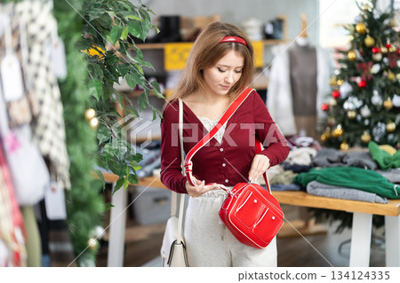 woman in a warm sweater chooses a handbag against the background of a Christmas tree woman in a warm sweater chooses a handbag against the background of a Christmas tree 134124335