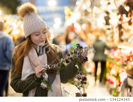 Girl looks at garland made of fir cones and brunchs, Xmas atmosphere Girl looks at garland made of fir cones and brunchs, Xmas atmosphere 134124345