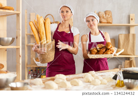 Portrait of two female professional baker in uniform standing and posing with fresh bakery goods in bakery during working day Portrait of two female professional baker in uniform standing and posing with fresh bakery goods in bakery during working day 134124432