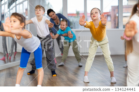 Positive juvenile girl engaged in Rock 'n' Roll dance in training room with children's group Positive juvenile girl engaged in Rock 'n' Roll dance in training room with children's group 134124441