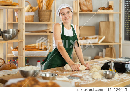Teenage girl baker kneads the dough in bakery Teenage girl baker kneads the dough in bakery 134124445