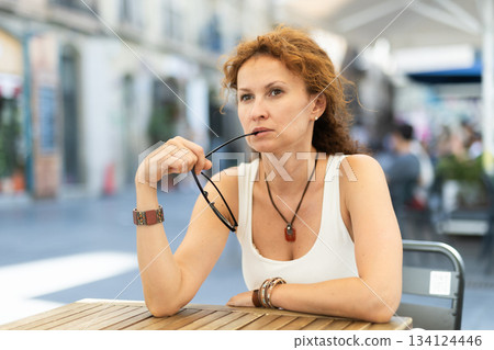 Thoughtful middle-aged woman sitting in open-air cafe Thoughtful middle-aged woman sitting in open-air cafe 134124446