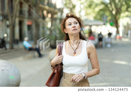 Woman with leather tote bag walking through summer city street Woman with leather tote bag walking through summer city street 134124473