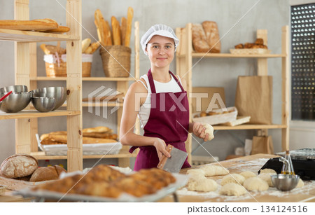 Teenage girl cutting dough on table in bakehouse Teenage girl cutting dough on table in bakehouse 134124516