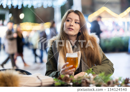 On winter outside of cafe, girl is relaxing at table, drinking beer 134124540