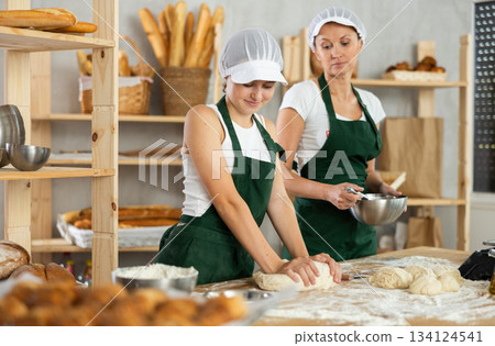 Two professional female baker in apron working in bakehouse, whips up and kneading dough 134124541