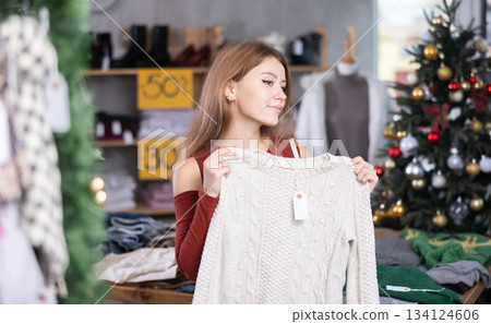 Girl client looks at products in store, looks closely at sweater, picks up wardrobe item Girl client looks at products in store, looks closely at sweater, picks up wardrobe item 134124606