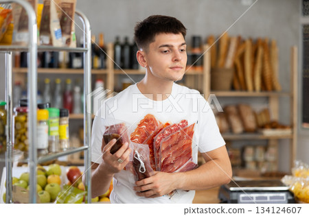 Young guy is choosing dried sausage and meat in grocery store Young guy is choosing dried sausage and meat in grocery store 134124607