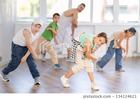 In sports studio, childrens team learns hip-hop dance accompanied by experienced man teacher In sports studio, childrens team learns hip-hop dance accompanied by experienced man teacher 134124621