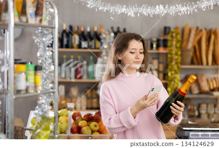 Female buyer purchaser scanning with smartphone QR code label of bottle of wine in shop Female buyer purchaser scanning with smartphone QR code label of bottle of wine in shop 134124629