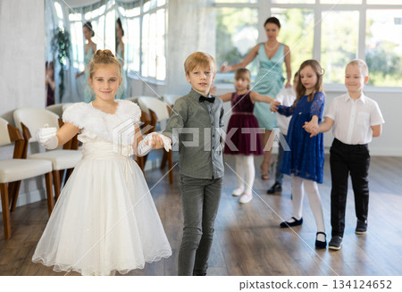 Little children in elegant dresses standing in pairs in dance pose in school hall Little children in elegant dresses standing in pairs in dance pose in school hall 134124652