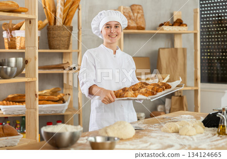 Young girl baker are standing near product range in bakery kitchen with basket loaf of croissants 134124665
