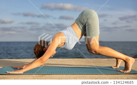 Yoga practice on embankment, female athlete fulfil carry out Adho Mukha Svanasana Yoga practice on embankment, female athlete fulfil carry out Adho Mukha Svanasana 134124685