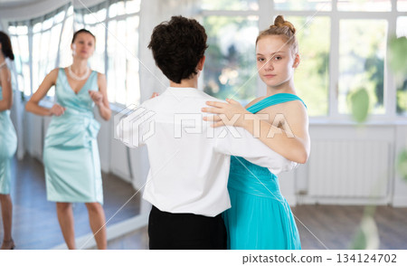 Girl and a boy in festive clothes learn to dance tango under guidance of teacher 134124702