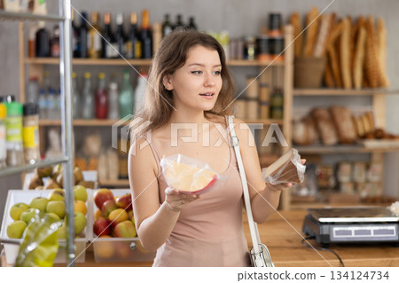 Female shopper chooses which cheese to buy at supermarket Female shopper chooses which cheese to buy at supermarket 134124734