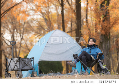 Male solo camper relaxing in a chair at autumn camp, having fun outdoors - looking at camera 134124874