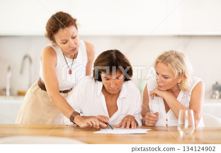 Three women help each other sort out financial documents in the kitchen of home Three women help each other sort out financial documents in the kitchen of home 134124902