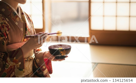 一幅日式房間場景，一位身穿和服的女子在新年當天吃年糕。 134125654