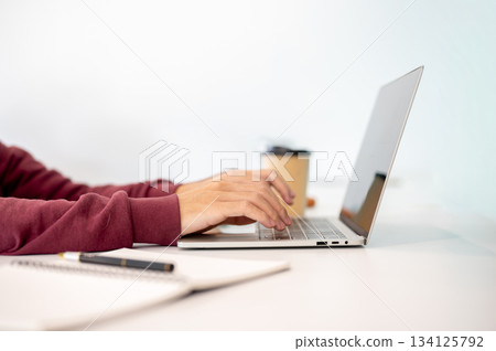 A man student's hands typing on laptop aside notebook and coffee on white table in a cafe or library A man student's hands typing on laptop aside notebook and coffee on white table in a cafe or library 134125792