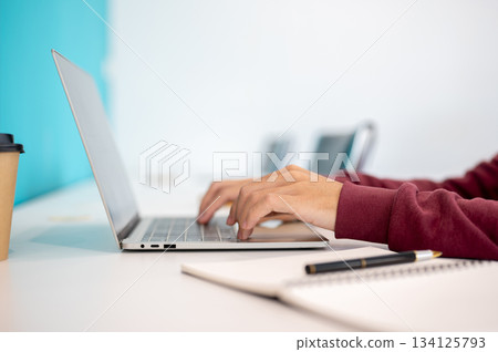 A male student's hands typing on laptop aside notebook and coffee on white table in cafe or library A male student's hands typing on laptop aside notebook and coffee on white table in cafe or library 134125793
