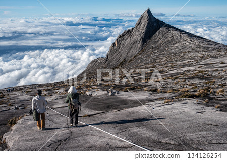 Rear view of tourist with an iconic peak named South Peak (3929 m) on Mt.Kinabalu, Malaysia. Mount Kinabalu is the tallest mountain in Malaysia and Borneo. Rear view of tourist with an iconic peak named South Peak (3929 m) on Mt.Kinabalu, Malaysia. Mount Kinabalu is the tallest mountain in Malaysia and Borneo. 134126254
