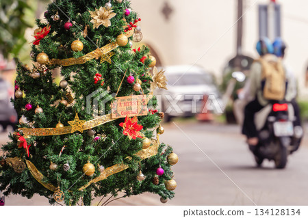 Christmas tree decorated with balloons and a yellow shiny ribbon with sequins on a Phuket street during the day in Thailand, near the road where vehicles and motorcycles drive. High quality photo 134128134