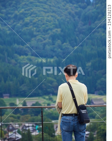 A middle-aged male tourist looking down on the scenery from the observation deck of Shirakawa-go, a World Heritage Site 134128213