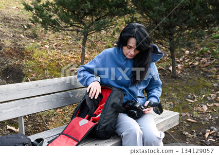 Russian woman 50 years old calmly packs her camera gear in a backpack, reflecting mindful preparation, respect for tools, and a sense of responsibility. 134129057