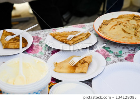 Traditional Russian pancakes served with butter during Maslenitsa festival. Paper plates on floral tablecloth, no people, spring celebration. 134129083