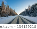 A tranquil winter road surrounded by snow-laden trees under a clear blue sky 134129218