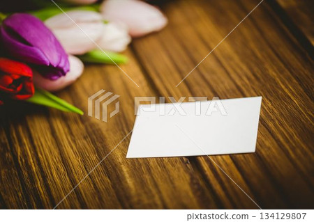 Blank white rectangular card is resting on flat design wooden tabletop, with red purple pink tulips 134129807