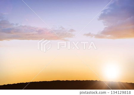 Sun disk is glowing near horizon, pastel clouds are drifting over ridge silhouette in flat design Sun disk is glowing near horizon, pastel clouds are drifting over ridge silhouette in flat design 134129818