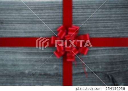 Red gift bow is sitting on grey wood surface in flat design, with crossed satin ribbons 134130056